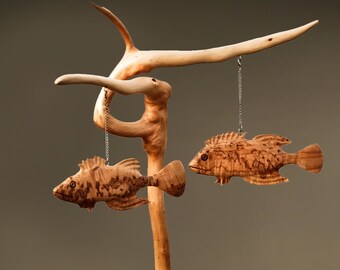 May include: A wooden sculpture of a tree with two carved fish hanging from it. The fish are brown and have detailed scales. The tree is on a wooden base.