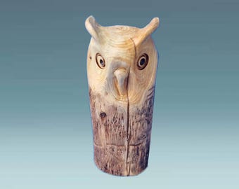 May include: A wooden owl sculpture carved from a tree trunk. The owl has a light brown color and is detailed with black eyes and a beak.