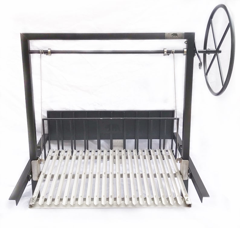 May include: A black metal rotisserie with a stainless steel grilling grate. The rotisserie has a large wheel on the right side for turning the spit. The spit is suspended from the top of the rotisserie frame by two chains.