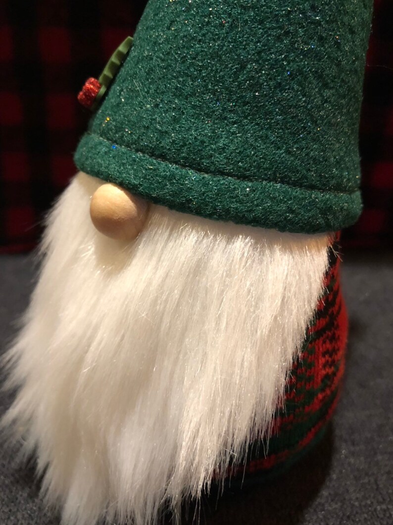 Peut inclure: Un chapeau de gnome en feutre vert avec une barbe en fourrure blanche et un corps en tartan rouge et vert.