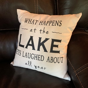 May include: White throw pillow with black text that reads "What happens at the lake gets laughed about all year".