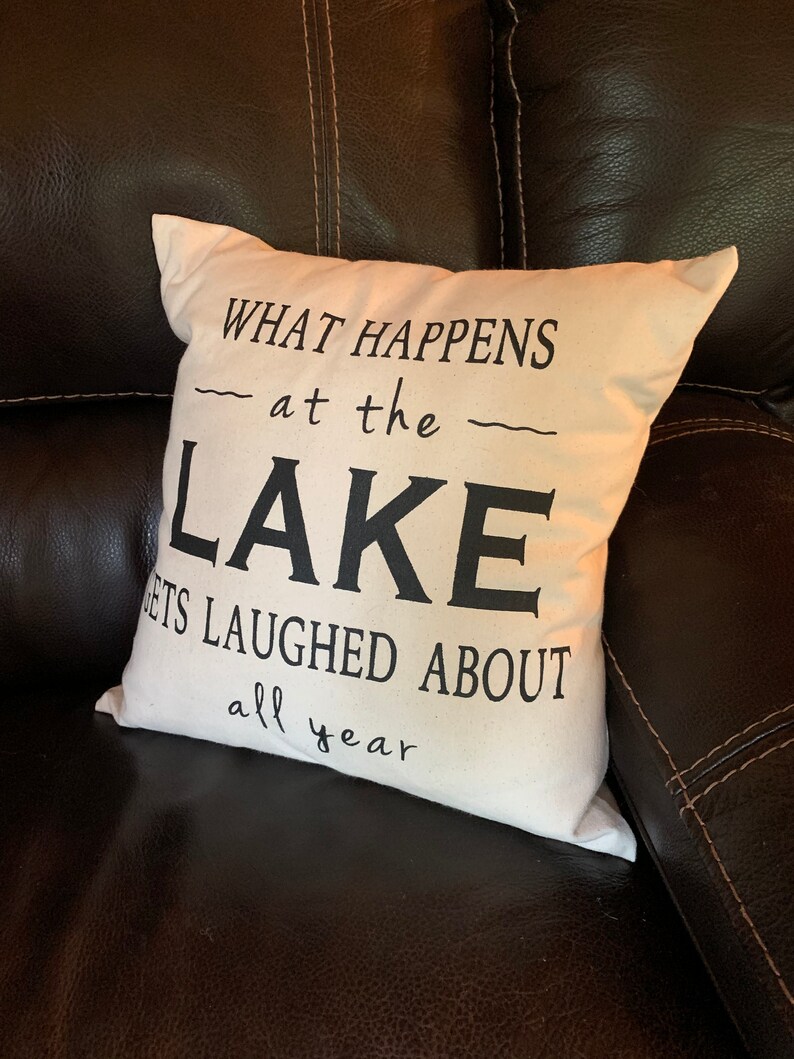 May include: White throw pillow with black text that reads "What happens at the lake gets laughed about all year".
