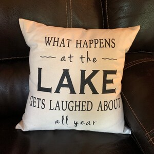 May include: White throw pillow with black text that reads "What happens at the lake gets laughed about all year".