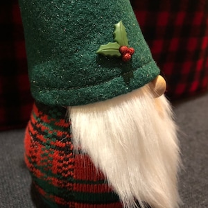 Peut inclure: Un gnome en feutre vert avec une barbe blanche et un corps en tartan rouge et vert. Le gnome porte un chapeau en feutre vert avec une branche de houx et des baies rouges.