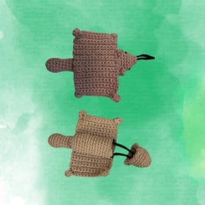 May include: Two crocheted bear-shaped toys in shades of brown and tan are displayed against a green background. The bears have outstretched arms, small ears, and a black string extending from their noses. The toys are handmade.