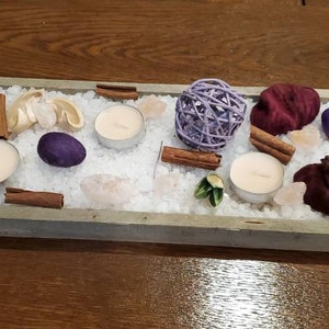 May include: A rectangular tray filled with white salt, cinnamon sticks, small purple and pink flowers, and three white candles. The tray is made of wood and has a distressed white finish.