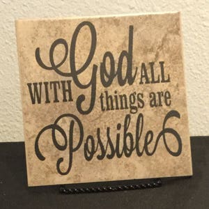 May include: A beige tile with a brown marbled pattern features a black cursive inscription that reads "With God all things are possible."