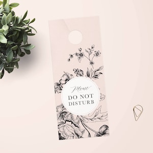 Op de afbeelding: Een roze deurhanger met een bloemenmotief en de tekst "Alstublieft niet storen".