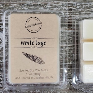 May include: A clear plastic package of six white soy wax melts, labeled "White Sage" with a drawing of a bundle of sage. The package also includes the text "Scented Soy Wax Melts 2.5oz (70.8g) Hand Poured in Douglassville, PA."