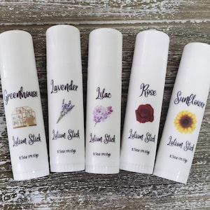 May include: Five white lotion sticks with labels featuring botanical themes. The labels display the names "Greenhouse," "Lavender," "Lilac," "Rose," and "Sunflower," along with illustrations of each. Each stick is 0.5 oz (14g).
