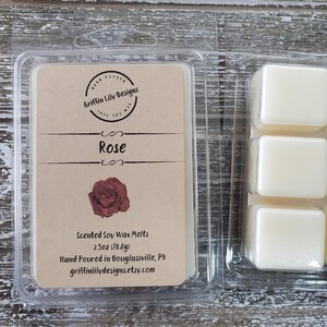 May include: Clear plastic packaging containing scented soy wax melts. The label reads "Rose" with a rose graphic. The package contains six square wax cubes. The label also includes the text "Griffin Lily Designs".