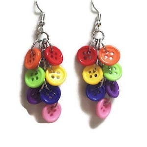 May include: A pair of colorful button earrings. Each earring features a cluster of vibrant, round buttons in shades of red, orange, yellow, green, blue, purple, and pink, suspended from a silver-tone hook.