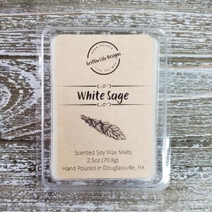 May include: A clear plastic container with a brown label that reads "Griffin Lily Designs" and "White Sage". The label also includes the text "Scented Soy Wax Melts 2.5oz (70.8g) Hand Poured in Douglassville, PA".