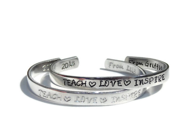 May include: Two silver bracelets with the inscription "Teach Love Inspire" and the year "2018". The bracelet on top also has the inscription "From Griffin".