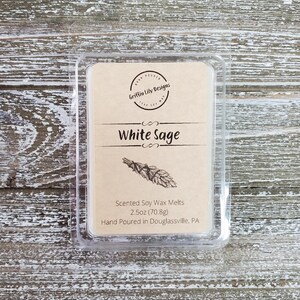 May include: A clear plastic container with a brown label that reads "Griffin Lily Designs" and "White Sage". The label also includes a drawing of a bundle of white sage and the text "Scented Soy Wax Melts 2.5oz (70.8g) Hand Poured in Douglassville, PA".