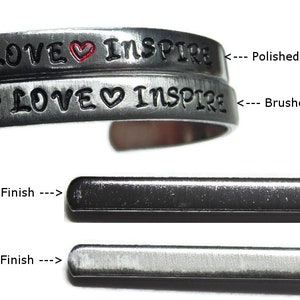 May include: Two silver bracelets with the words "LOVE" and "INSPIRE" engraved on them. The top bracelet has a polished finish, while the bottom bracelet has a brushed finish.