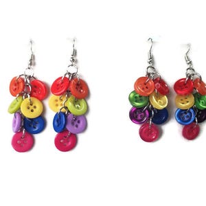 May include: Two pairs of handmade button earrings. Each earring features a cluster of colorful buttons in shades of red, orange, yellow, green, blue, purple, and pink. The earrings hang from silver-colored hooks.