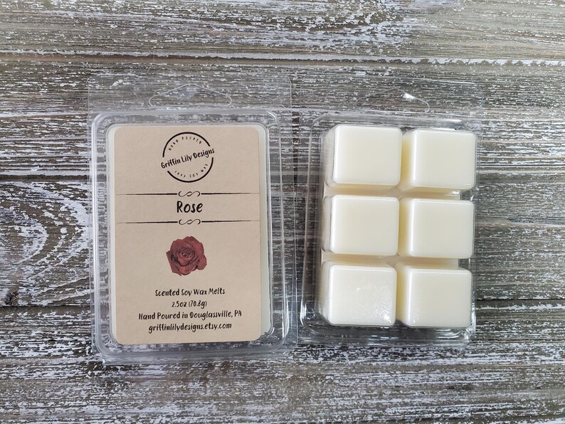 May include: A clear plastic container holding six square wax melts and a label. The label reads "Rose" with a rose graphic and product details. The wax melts are a creamy white color. The product is 2.5oz (70.8g).