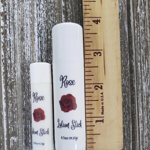 Pode incluir: Duas barras de lo&ccedil;&atilde;o brancas com a inscri&ccedil;&atilde;o "Rose Lotion Stick" e uma rosa vermelha. A barra maior tem cerca de 10 cm de altura, e a menor 5 cm. A barra maior cont&eacute;m 14,17 g.