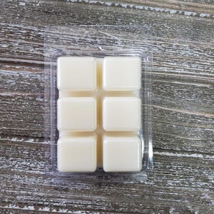 May include: A clear plastic tray with six square wax melts. The wax melts are white and are arranged in a 2x3 grid.