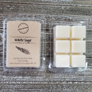May include: A clear plastic container of six white soy wax melts, labeled "White Sage" with the text "Scented Soy Wax Melts 2.5oz (70.8g) Hand Poured in Douglassville, PA".