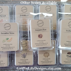 May include: A collection of 12 small, clear plastic containers filled with scented soy wax melts. Each container has a label with a different scent name and a small image. The scents include: Autumn Harvest, Greenhouse, W, Cinnamon Bun, Frooty Cereal, Cucumber Melon, Lavender, Sea Shell, Coffee, Oatmeal Raisin Cookies, and Lilac. The containers are arranged in a grid pattern on a wooden surface. The text "Griffin Lily Designs.etsy.com" is printed at the bottom of the image.