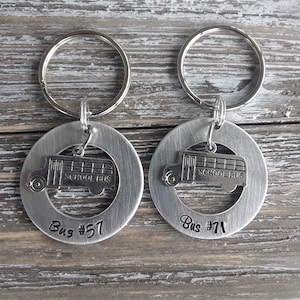 May include: Two silver keychains with a school bus cutout design. One keychain says "Bus #57" and the other says "Bus #71".