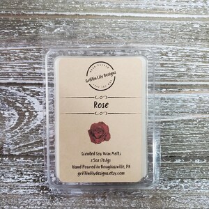 May include: A clear plastic clamshell package containing a scented soy wax melt. The label is tan with the word "Rose" and a red rose illustration. The package contains 2.5oz (70.8g) of wax melts.