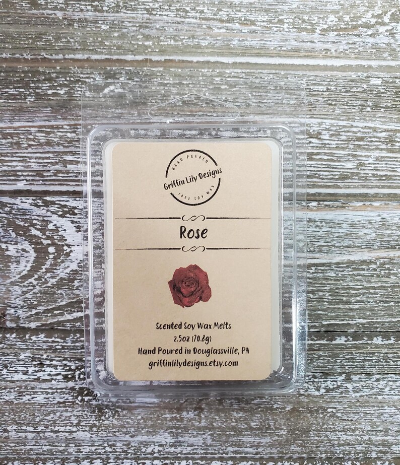 May include: A clear plastic clamshell package containing a scented soy wax melt. The label is tan with the word "Rose" and a red rose illustration. The package contains 2.5oz (70.8g) of wax melts.