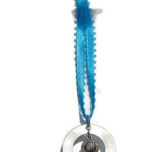 May include: A silver-toned circular metal charm engraved with the name Jamie and the number 23, featuring a small three-dimensional basketball charm suspended in the center, all attached to a bright blue ribbon with a decorative picot edge.