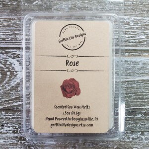 May include: A clear plastic clamshell package containing a scented soy wax melt. The label is tan with the text "Rose" and a red rose illustration. The package is 2.5oz (70.8g) and hand-poured by Griffin Lily Designs.