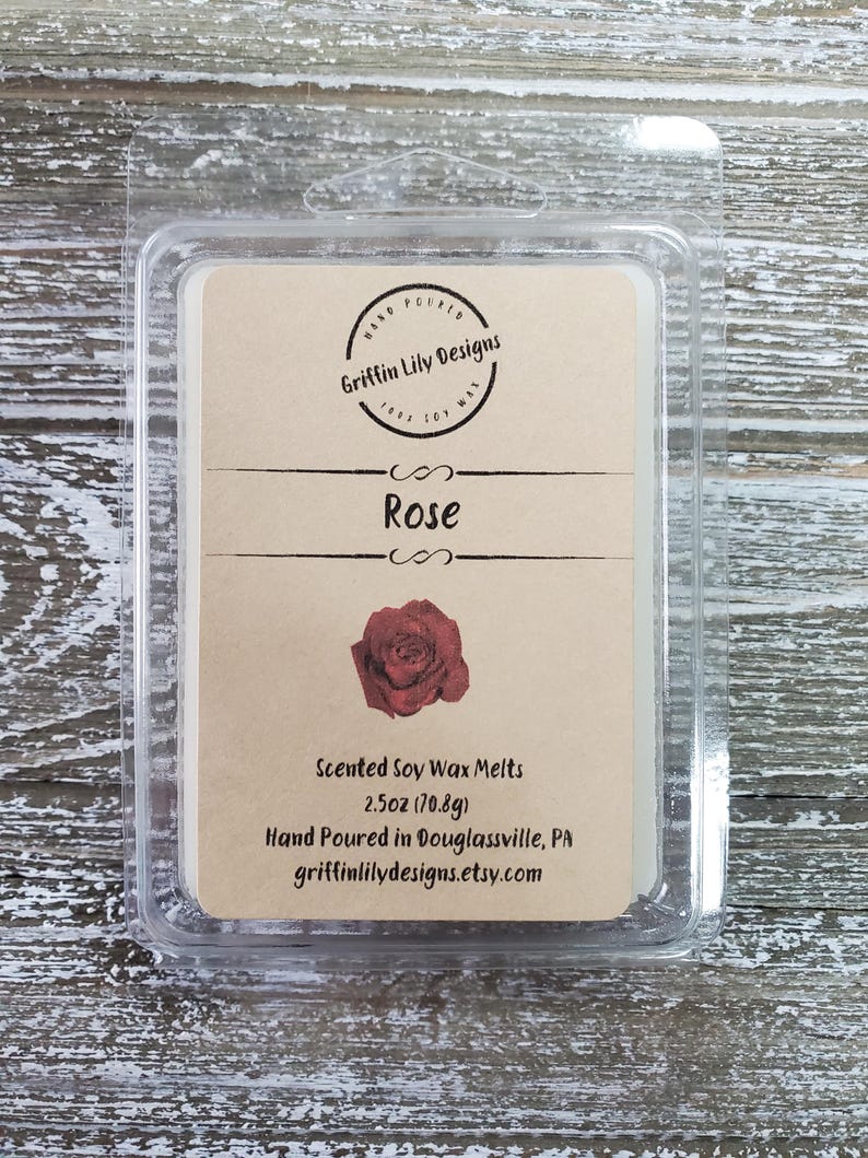 May include: A clear plastic clamshell package containing a scented soy wax melt. The label is tan with the text "Rose" and a red rose illustration. The package is 2.5oz (70.8g) and hand-poured by Griffin Lily Designs.