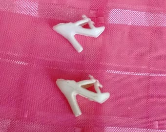 May include: Two small, white high-heeled shoes with delicate straps. The shoes are set against a bright pink, textured background, creating a contrast in color and texture. The heels are a classic stiletto style.