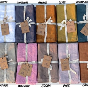 K&ouml;nnte beinhalten: Set mit 14 Leinenservietten in verschiedenen Farben, darunter Chambray/Anthrazit, Wei&szlig;, Anthrazit, Bernstein, Oliv, Ozeanblau, Ton, Chambray/Denim, Natur, Wildrose, Kakao, Feigen, Kamel und Blau. Jede Serviette ist mit einem Band gebunden und hat ein kleines Etikett mit dem Markennamen.