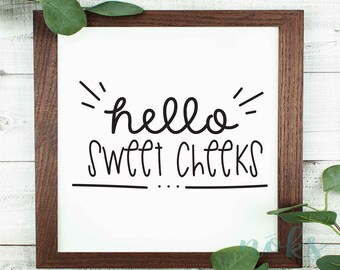 May include: A white framed sign with black lettering that reads "hello sweet cheeks" with a decorative flourish above the word "hello".