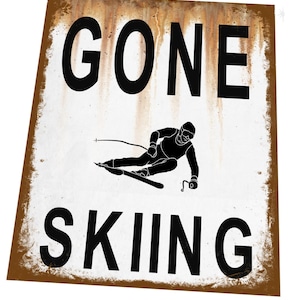 May include: A white metal sign with brown rust-like markings. The sign says "GONE SKIING" in black text with a silhouette of a skier in the middle.