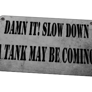 Op de afbeelding: Een grijs metalen bord met zwarte tekst die luidt "DAMN IT! SLOW DOWN A TANK MAY BE COMING".