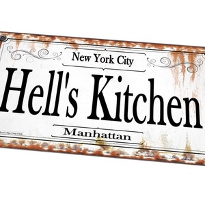 May include: A white metal sign with rusty edges and black text that reads "New York City", "Hell's Kitchen", and "Manhattan".
