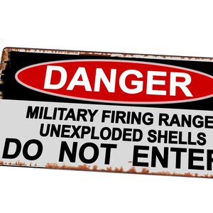 Op de afbeelding: Een wit metalen bord met zwarte en rode letters. Het bord luidt "GEVAAR MILITAIR SCHIETBAAN ONGEEXPLODEERDE GRANATEN NIET BETREDEN".