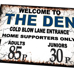 Peut inclure: Une pancarte blanche avec du texte noir qui indique "Bienvenue au Den Cold Blow Lane Entrance Home Supporters Only Adults 85p Juniors 30p". La pancarte a un aspect vieilli et rouillé et comporte deux flèches noires pointant vers le bas.