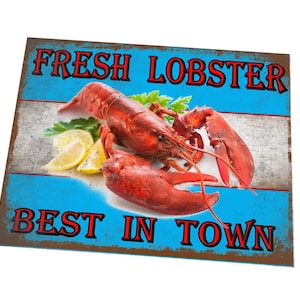 Könnte beinhalten: Ein Schild im Vintage-Stil mit blauem Hintergrund und rotem Text, der "FRESH LOBSTER BEST IN TOWN" lautet. Auf dem Schild ist ein gekochter Hummer mit Zitronenscheiben und Petersilie abgebildet.