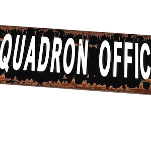 Op de afbeelding: Een zwart en bruin metalen bord met witte tekst die "Squadron Office" aangeeft.
