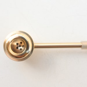 K&ouml;nnte beinhalten: Eine goldene Metall-Rauchpfeife mit einer runden Schale und einem langen, geraden Schaft. Die Schale hat eine Reihe kleiner L&ouml;cher f&uuml;r den Luftstrom. Der Schaft hat ein klares Plastikmundst&uuml;ck.
