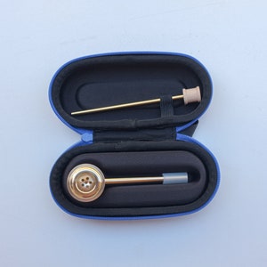 K&ouml;nnte beinhalten: Eine blaue Tragetasche mit einer goldenen Pfeife aus Metall und einem langen, d&uuml;nnen Werkzeug aus goldfarbenem Metall im Inneren. Die Tasche ist ge&ouml;ffnet und die Pfeife und das Werkzeug sind sichtbar.