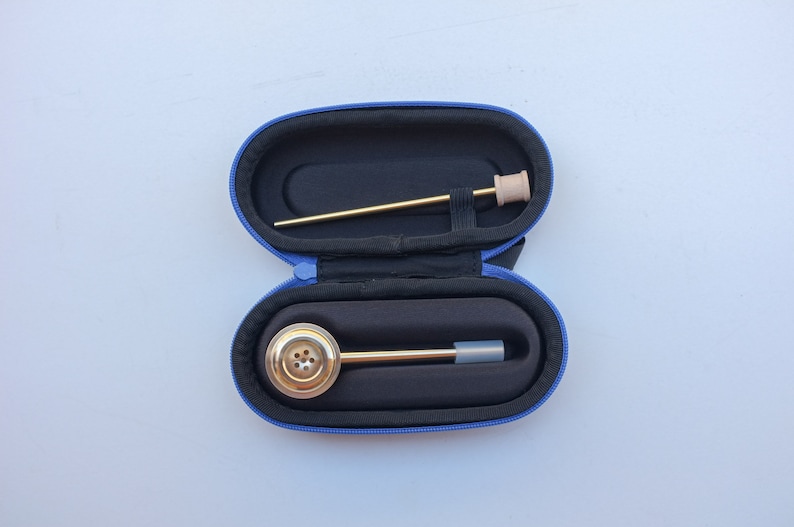 K&ouml;nnte beinhalten: Eine blaue Tragetasche mit einer goldenen Pfeife aus Metall und einem langen, d&uuml;nnen Werkzeug aus goldfarbenem Metall im Inneren. Die Tasche ist ge&ouml;ffnet und die Pfeife und das Werkzeug sind sichtbar.