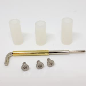 May include: An assortment of hardware components, including three small, silver screws, three white cylindrical sleeves, and a gold and silver Allen wrench. The items are arranged on a white surface.