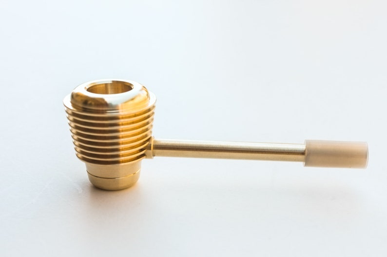 K&ouml;nnte beinhalten: Eine goldene Metallpfeife mit geripptem Design und einem Mundst&uuml;ck. Die Pfeife hat einen langen, geraden Schaft und eine kleine, runde Schale.
