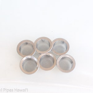 Puede incluir: Seis pantallas de metal plateado para una pipa para fumar. Las pantallas son redondas y tienen un diseño de malla.
