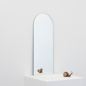 May include: A gold snail sculpture sits on a white surface in front of a tall, arched mirror. The mirror reflects the snail.