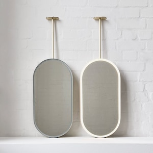 May include: Two oval-shaped mirrors with gold metal frames and hanging rods. The mirror on the left has a silver backing, while the mirror on the right has a white backing.